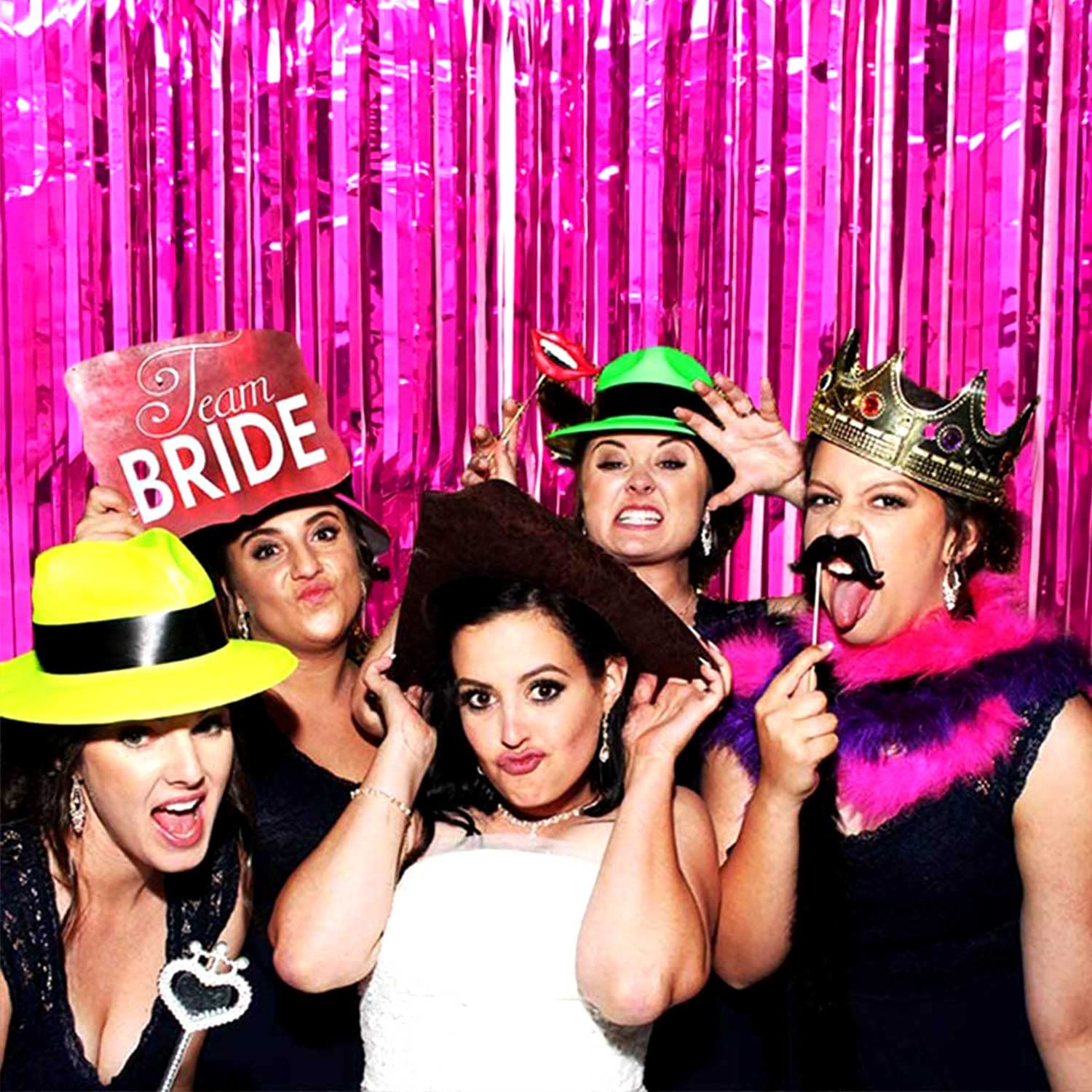 “Friends posing in front of fuchsia fringe backdrop”